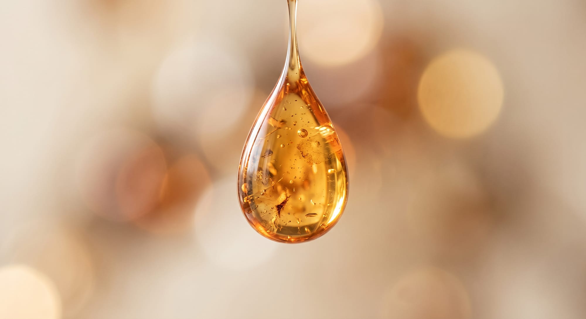 A single amber droplet suspended in soft golden light