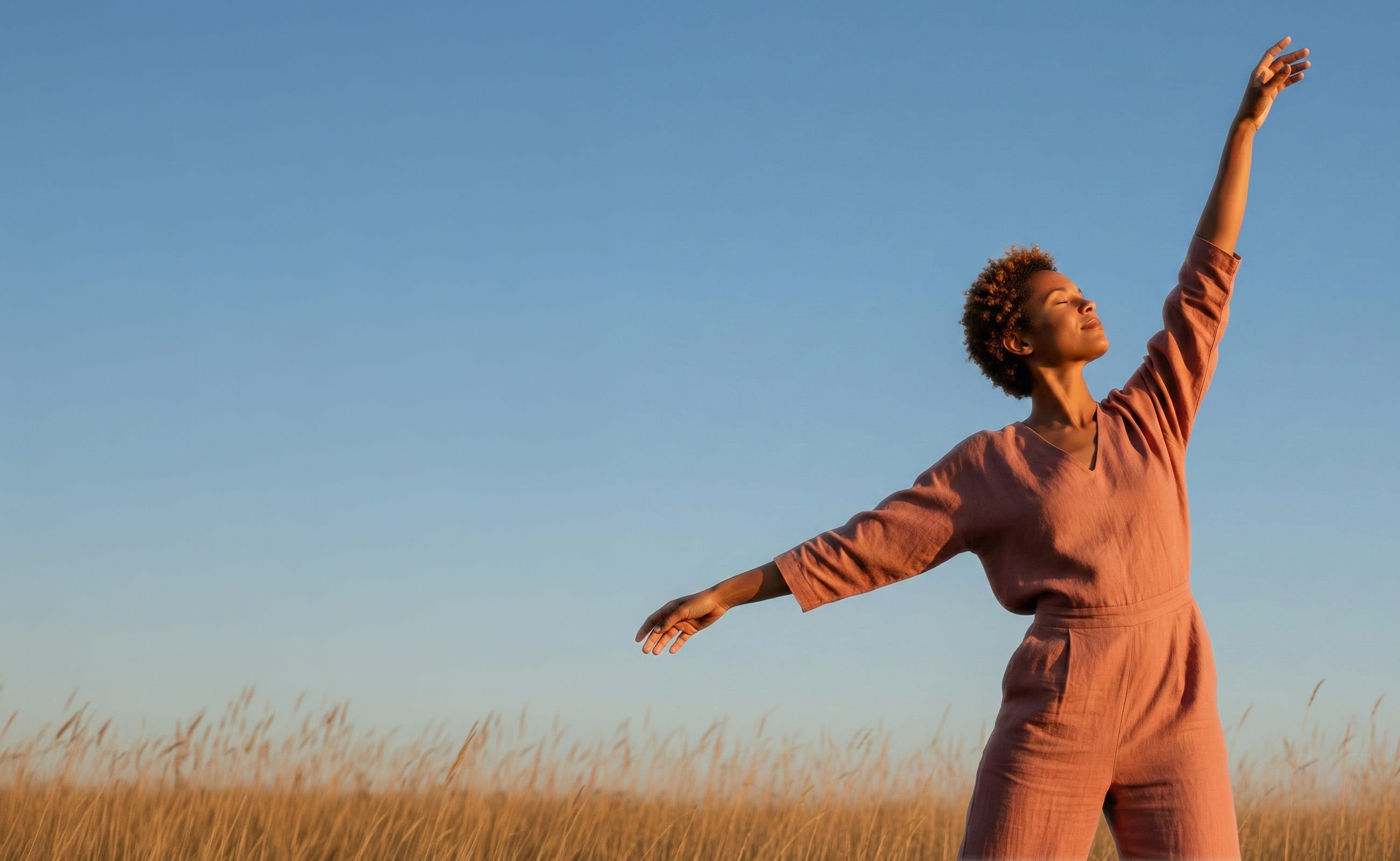 A woman standing in a golden field, arms raised